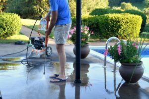 A man power washing the dirt off the cement pool deck at home.
