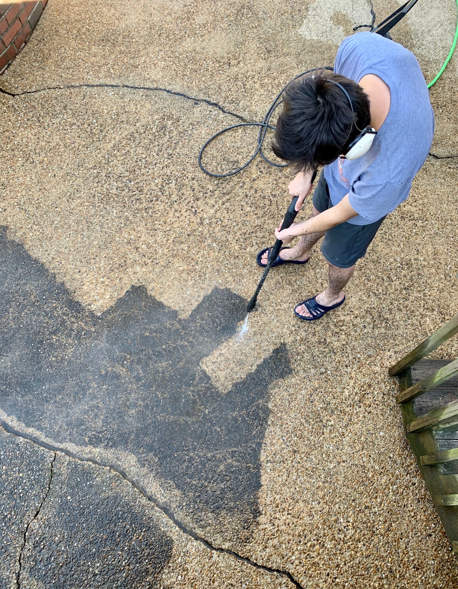 Overhead of a young GenZ adult man doing house chores power washing the ...