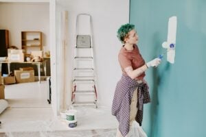 Young adult woman painting wall with roller brush during home renovation